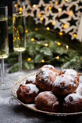 Oliebollen traditional Dutch New Year's Eve pastry dusted with powder sugar served with champagne. New year lights bokeh and sparkles on background.
