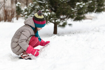 Fototapeta na wymiar Playing in the snow. The girl kid child in warm waterproof winter suit in waterproof mittens plays in the snow outside 