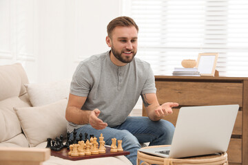 Fototapeta na wymiar Young man playing chess with partner through online video chat at home
