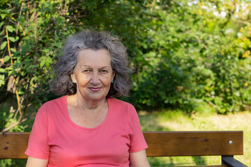 An elderly woman with gray hair, freckles and wrinkles on her face. Grandmother in a bright t-shirt smiling while looking at the camera.