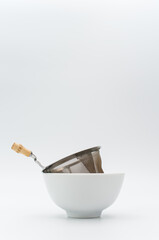metal tea strainer in a white stoneware bowl on a white tabletop background