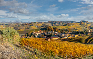 Landscape on the hills of the Barolo area, Langhe, Italy, with Barolo Village and Castle, fine vineyards of Nebbiolo grapes with autumn colors on blue sky with cloud
