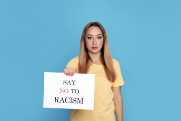 Young woman holding sign with phrase Say No To Racism on light blue background