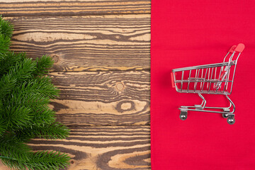 Small trolley, mini shopping cart, Christmas tree branch on wooden background. New year fair, market, sale concept