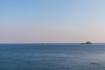 Obraz premium The blue sea with sunset, two lighthouses and a small island.