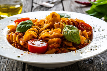 Fusilli with minced meat, tomato sauce, parmesan cheese and basil served on wooden table
