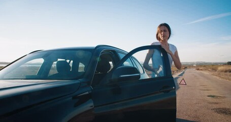 Vehicle breakdown on travel young attractive woman driver outs of the car opening hood and checking the failure of car. Cinematic real time footage on evening on country road