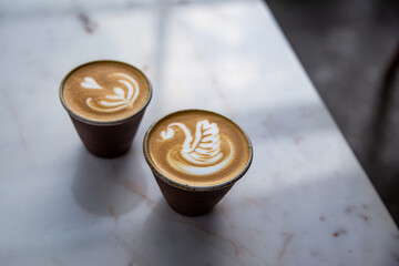 Two beautiful cups of cappuccino with latte art on table.