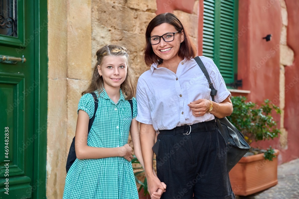 Poster outdoor portrait of mom and daughter 10, 11 years old on the street of old city looking into the cam