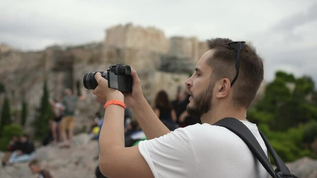 Young adult men among crowd of tourists spending time on taking pictures of historical Greek landmark. Traveler on sight of Acropolis in Athens. Tourism and traveling to ruins of ancient civilization.