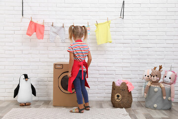 Little girl playing with toy cardboard washing machine indoors