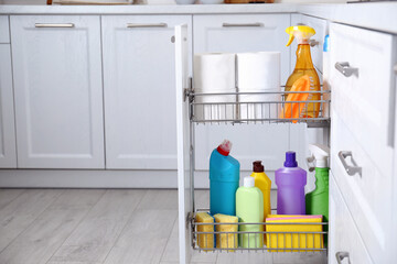 Open drawer with different cleaning supplies in kitchen, space for text