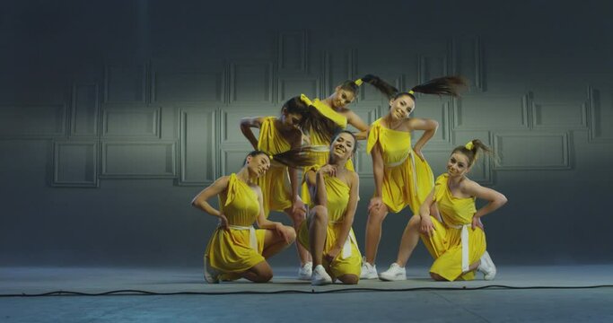 4k Group of beautiful , funny, stylish girls in yellow dresses dancing inside pavilion with grey background  . Synchronized dance of female ensemble for video clip  Woman dancers with the same outfit 