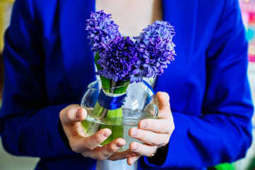 Redhead girl in a suit holds a vase with hyacinths in her hands