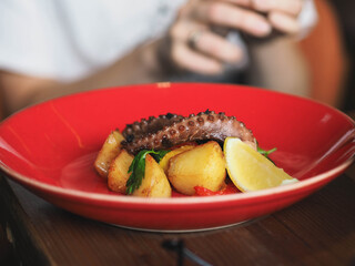 Fried octopus with potatoes on red plate in restaurant.