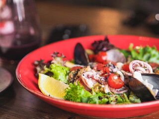 Fresh mediterranean seafood salad with olive oil, lemon, tomatoes and lettuce in red plate