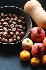 Pan with chestnuts, butternut squash and various fruit on dark background. Selective focus.