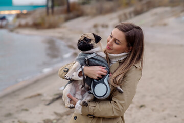 Young beautiful girl walks in the cold season on the beach with her pug dog