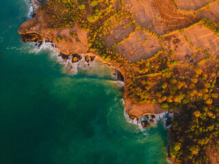 Aerial view of rocky shore with surfers, waves and sunset.
