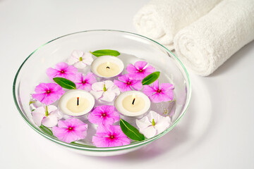 Burning floating candles with pink flowers in a bowl of water and two white towels, spa relaxation, body care and wellness