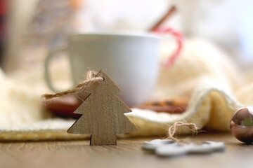 Cup of warm drink with candy cane and cinnamon stick, soft blanket and various Christmas decorations. Hygge at home. Selective focus.
