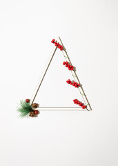 Christmas triangle frame with christmas red berries, pine branch and ornaments on white background. Minimal winter holidays and New Year idea.