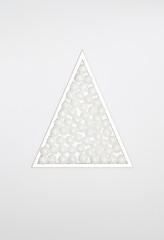 Christmas triangle frame filled with sparkle snow ornaments on white background. Minimal winter holidays and New Year concept.