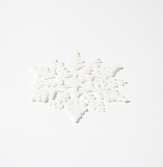 Christmas white snowflake with sparkle on white table. Minimal winter holidays and New Year monochrome aesthetic background.