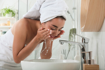 Beautiful young woman washing her face with water in bathroom