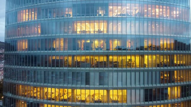 Office style concept. Working hours in the office building at night. Drone flight around the office skyscraper, UHD, 4K