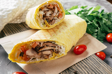 Classic shawarma with chicken and vegetables in pita bread on wooden dark background with cherry...