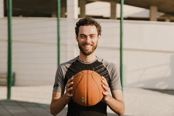 Young white man smiling while working out with ball on sports ground