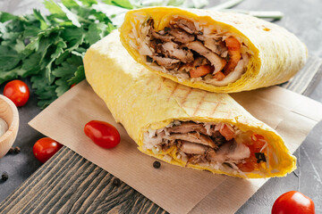 Classic shawarma with chicken and vegetables in pita bread on wooden dark background with cherry tomatoes and parsley