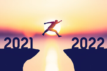 Silhouette man jumping between cliff with number 2021 to 2022 at tropical sunset beach. Freedom...