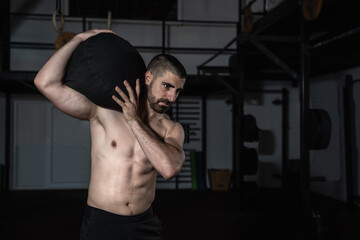 Fototapeta na wymiar Young strong sweaty fit muscular man with big muscles holding heavy sandbag exercise equipment with his hands as hardcore deadlift workout training in the gym. Real people 