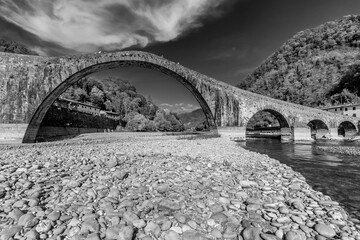 Ancient Ponte della Maddalena or Devil's bridge in black and white, under a dramatic sky, Borgo a...
