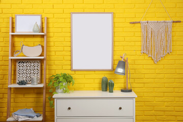 Empty frame hanging on yellow brick wall indoors. Mockup for design