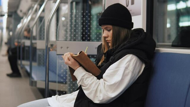 Talented artistic female drawing painting in metro using sketchbook and pencil. Young relaxed female artist drawing while traveling in metro subway tube underground 