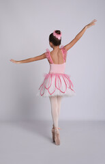 Beautifully dressed little ballerina dancing on grey background, back view © New Africa