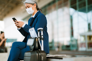 Fototapeta na wymiar Grey asian woman in face mask using cellphone while sitting on bench