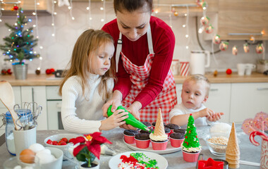 Brother and sister making cupcakes with their mom