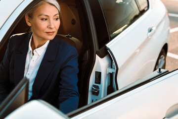 Mature businesswoman with grey hair getting out car