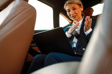 Mature asian businesswoman gesturing and working with laptop in car