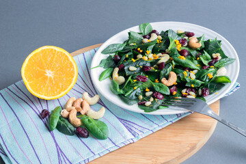 Vitamin fresh salad of spinach leaves, pine nuts, dried cranberries, cashews, zest and orange juice on a white plate. 