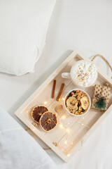 Christmas breakfast on a white wooden tray decorated with festive decor and garland. Breakfast in bed for Christmas. Christmas at the hotel. Vertical photo