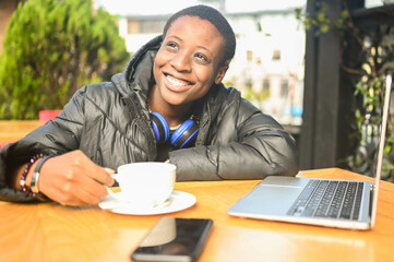 Smiling happy African black short-haired woman student in black down jacket with blue headphones...