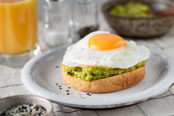 Breakfast avocado sandwich with fried egg and glass of orange juice on table, closeup view, selective focus