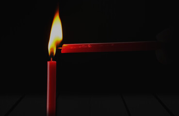 Red candle is lit with the light of yellow candle flame on black background. Ideas for Halloween,...