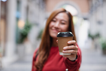 A young asian woman holding and showing a cup of coffee while traveling and sightseeing around the city