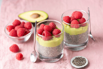 Vegan chia seed pudding with avocado mousse and raspberries in glass on pink textile background, closeup view healthy dessert